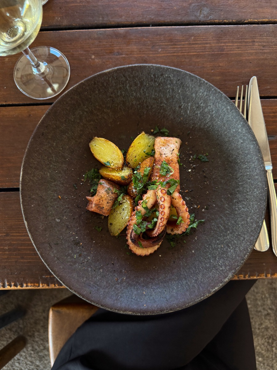 Pulpo a la brasa con patatas en un plato de cerámica sobre una mesa de madera